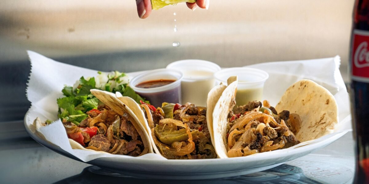a plate of tacos with a lime being drizzled on top