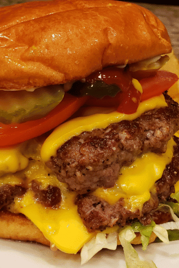 Juicy cheeseburger with pickles, tomatoes, and lettuce, served with potato chips.