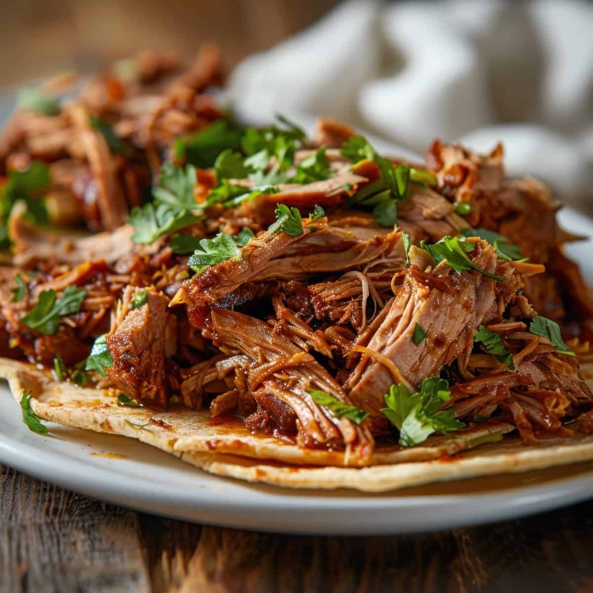 Juicy shredded beef tacos garnished with cilantro on a white plate.