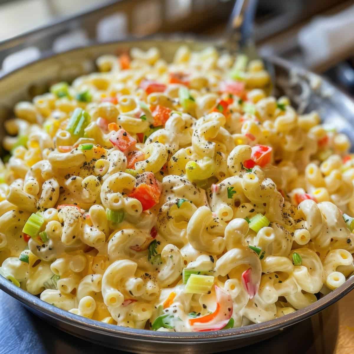 Creamy macaroni salad with colorful vegetables and herbs, served in a large bowl. Perfect for gatherings and casual meals.