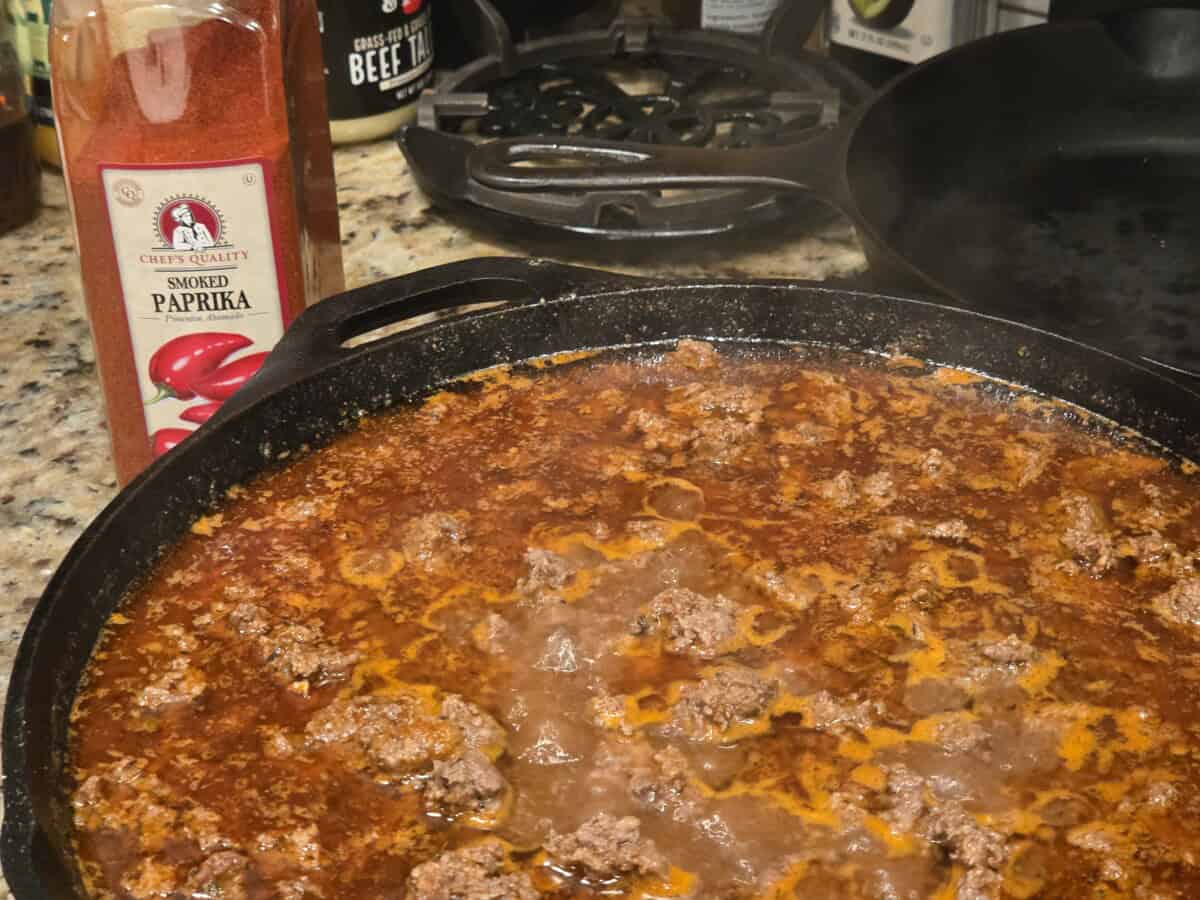 Cast iron skillet with smoked paprika ground beef simmering, Chef's Quality Smoked Paprika bottle in foreground, beef tallow jar visible in background.