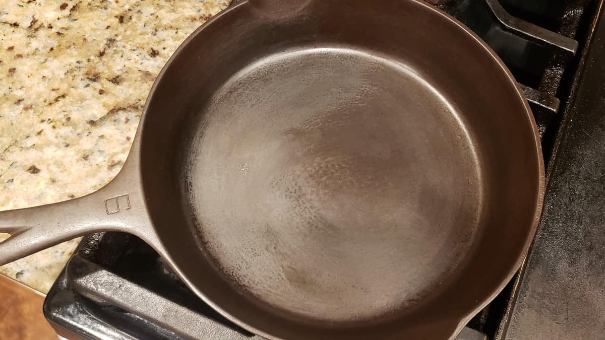Empty cast iron skillet on stove for batch cooking or preparation.